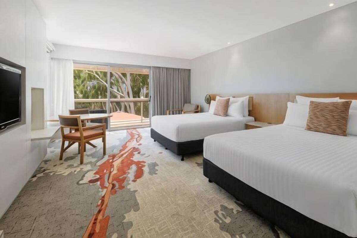 Habitación de hotel con dos camas, un escritorio, un televisor y un balcón con vistas.
