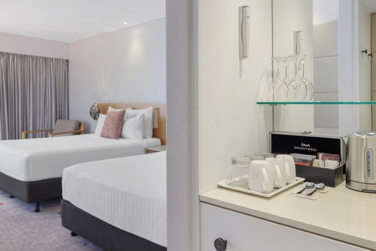 A hotel room with two beds, a desk with a mirror, and a tray with cups and a kettle.