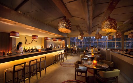 A bar area with a long counter, multiple hanging pendant lights, and a barista preparing drinks.