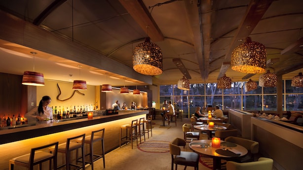 Una zona de bar con una barra alargada, varias luces colgantes y un barista preparando bebidas.