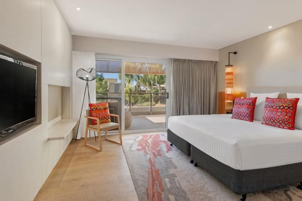 A hotel room with a bed, a TV, a chair, a balcony, and a view of the outdoors.