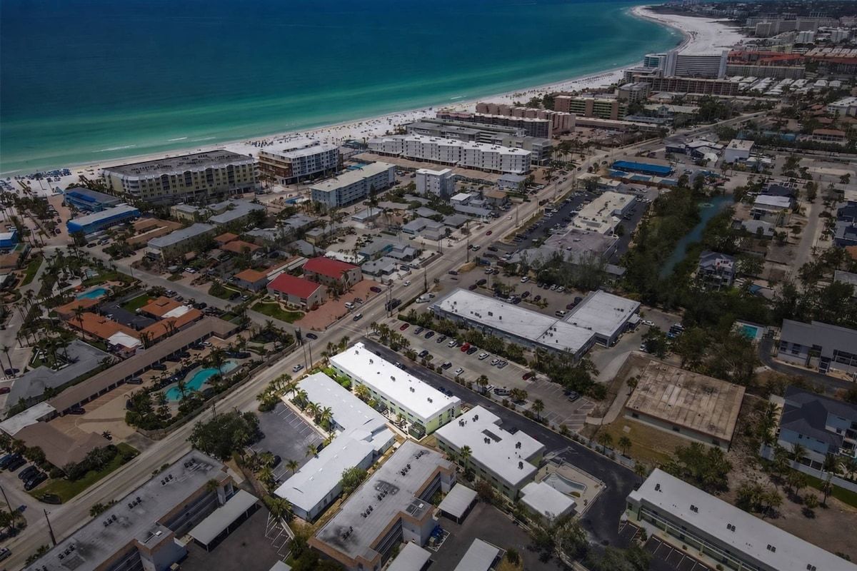An aerial view of a coastal city with a beach, hotels, and commercial buildings.