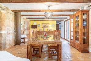 A dining area with a wooden table and chairs, a hanging light fixture, and a cabinet with glass doors. - Ca'n Corro – Exclusive Villa with Private Pool and Garden near Alcúdia & Playa de Muro (Alcudia)