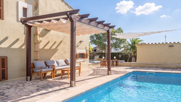 A pool area with a pergola, lounge chairs, and a tiled pool.