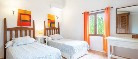 A room with two beds, a desk, a window with curtains, and artwork on the walls.