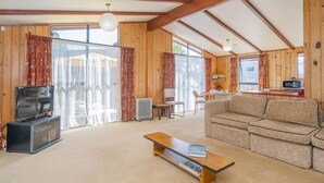 A cozy living room with a sofa, a coffee table, a TV, and a dining area with chairs and a table. - Sheppard's Rest - Pauanui Holiday Home (Pauanui)