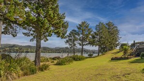 A grassy area with trees and a lake in the background. - Sheppard's Rest - Pauanui Holiday Home (Pauanui)