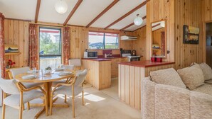 A cozy cabin interior with a wooden dining area, a kitchenette, and a living space with a sofa. - Sheppard's Rest - Pauanui Holiday Home (Pauanui)