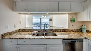 A kitchen with white cabinets, a granite countertop, a stainless steel sink, and a dishwasher. - Ocean Harbor #1201B Beautiful Bayfront Condo (Fort Myers Beach)