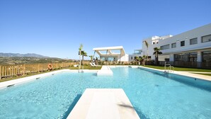 A modern hotel with a large swimming pool, a wooden deck, and a view of the mountains.