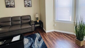 A living room with a brown leather sofa, a blue and white rug, and a small side table with a lamp.