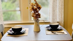 A dining table with two black bowls and a white vase with dried leaves.