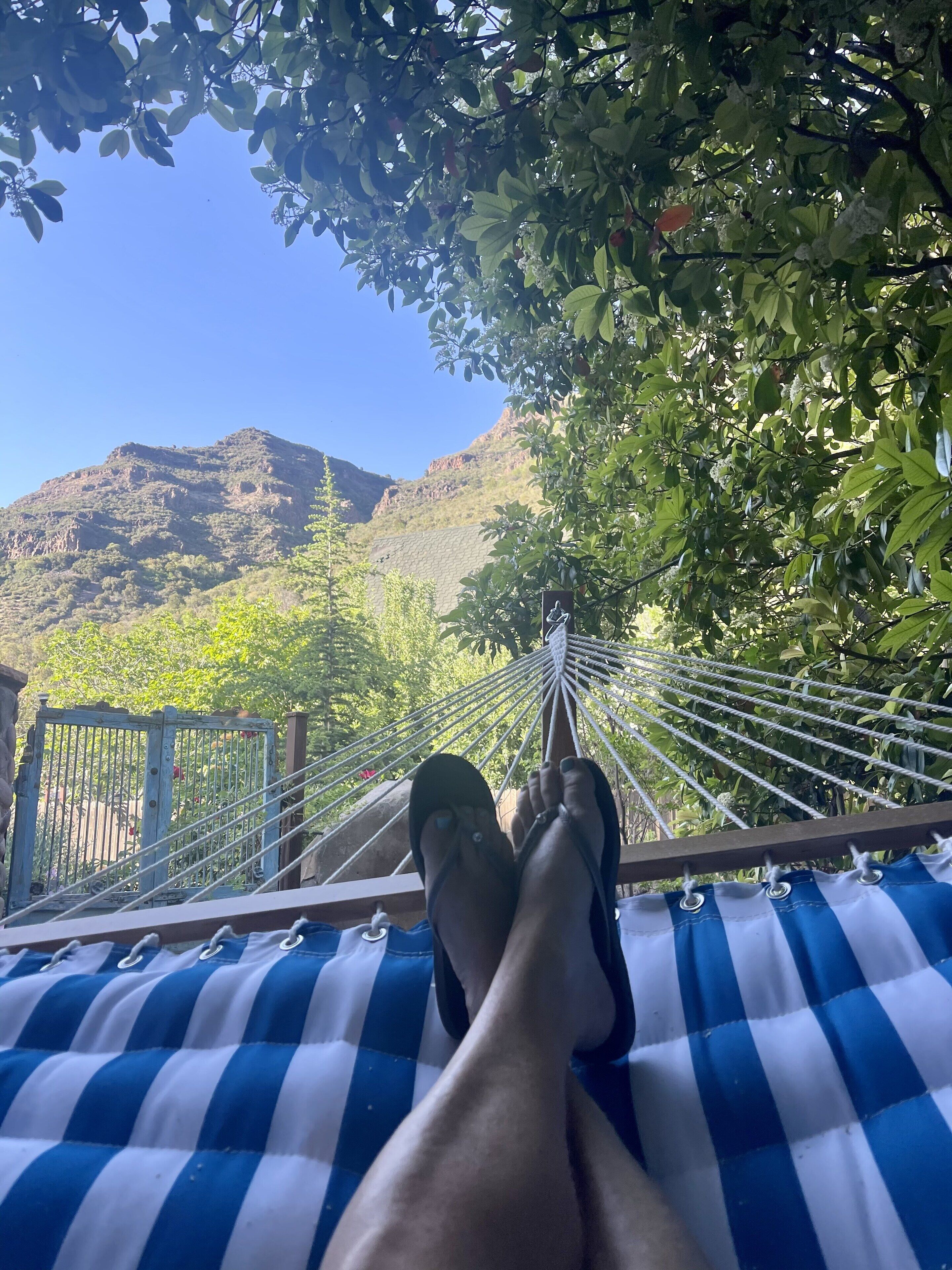 A hammock with a blue and white striped fabric, set against a backdrop of lush greenery and a mountainous landscape.