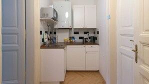 A compact kitchen with white cabinets, a microwave, a coffee maker, and a sink.