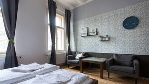 A room with two beds, a small table, two armchairs, a clock, and a window with curtains.