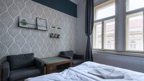 A hotel room with a bed, two armchairs, a small table, a window with curtains, and a patterned wallpaper. - Great room near city centre - private bathroom (Prague 2)