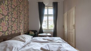 A bedroom with a bed, a small table, a chair, a window with curtains, and a door. - Wonderful room downtown with ensuite bathroom (Prague 2)