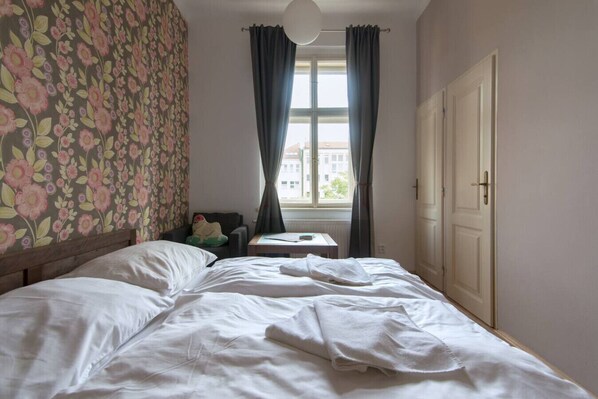 Une chambre à coucher avec un lit, une petite table, une chaise, une fenêtre avec des rideaux et une porte.