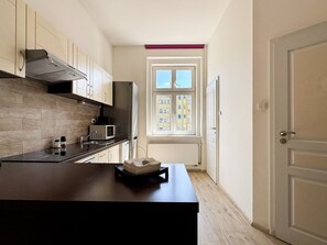 A modern kitchen with a dark countertop, a built-in stove, and a window with a view of buildings. - Two-bedroom apartment in Vinohrady (Prague 2)