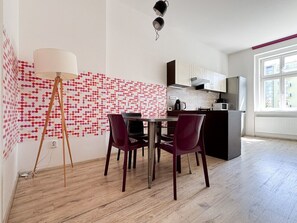 A modern kitchen with a dining area, featuring a patterned wall, a floor lamp, and a view of the city.