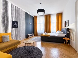 A modern hotel room with a bed, a sofa, a small table, and a hanging light fixture. - Two-bedroom apartment in Vinohrady (Prague 2)