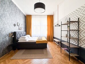 A modern bedroom with a bed, a bedside table, a hanging light, a bench, and a wall-mounted shelf.