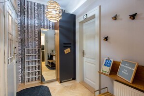 Um corredor com um espelho, uma porta, uma prateleira com uma placa e um lustre.
