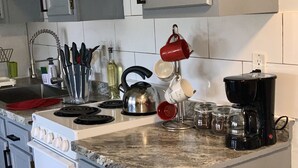 Een keuken met een fornuis, waterkoker, koffiezetapparaat en diverse keukengerei.