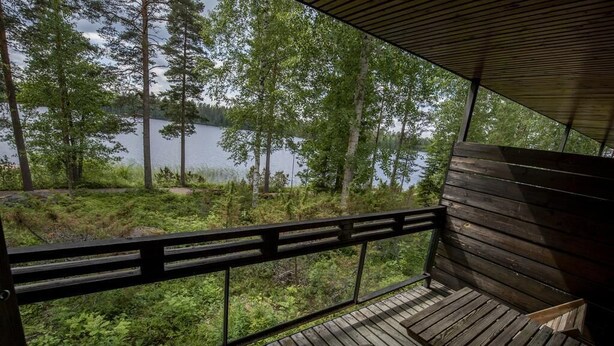 Una terraza de madera con un banco que da a un lago rodeado de árboles.