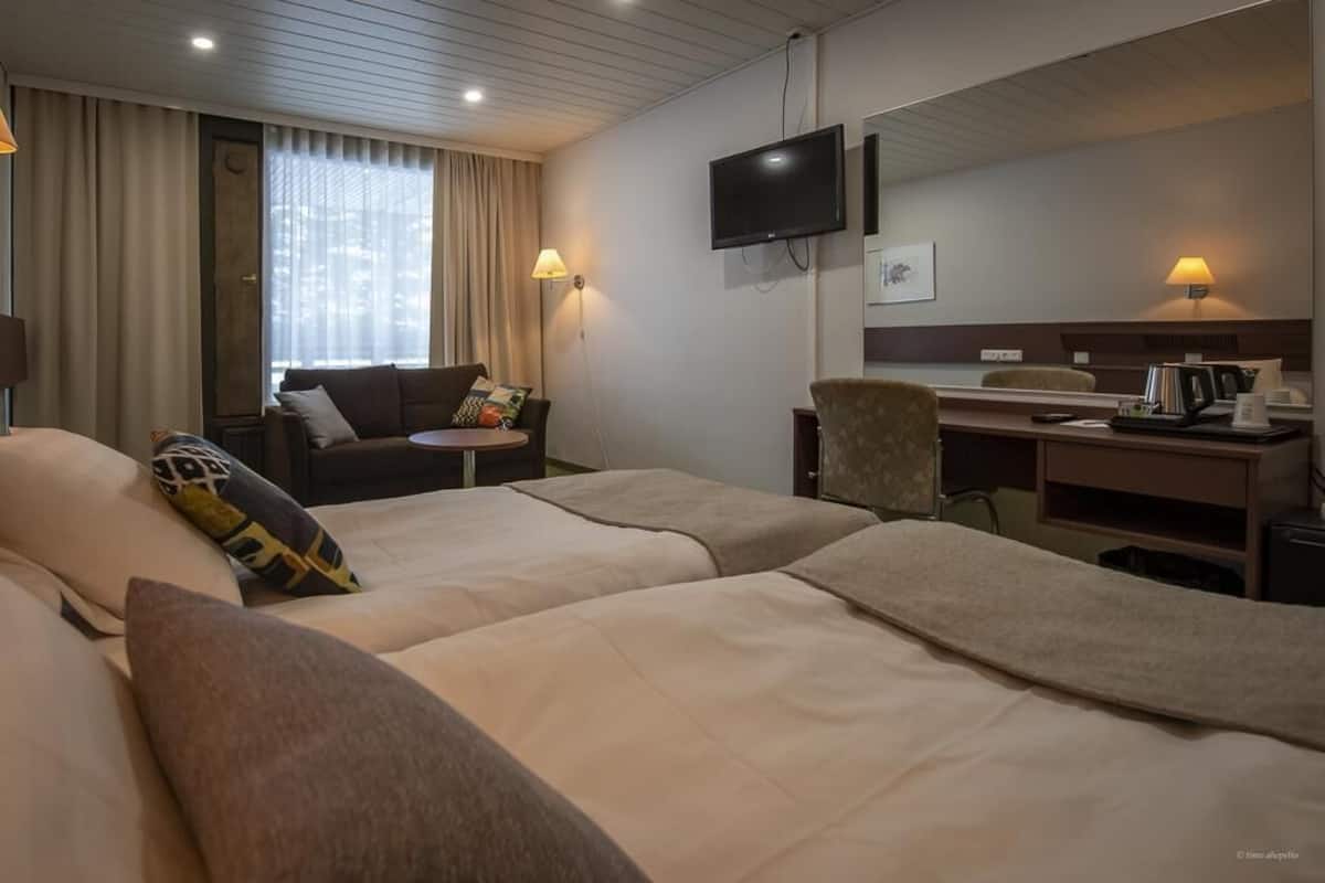A hotel room with two beds, a desk, a chair, a TV, and a window with curtains.