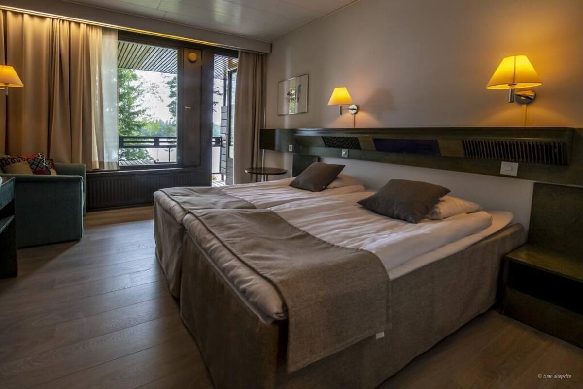 A hotel room with two beds, a sofa, a small table, and a window with curtains.