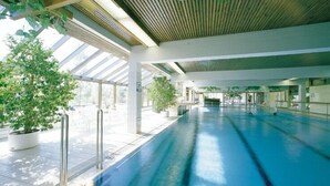 Una piscina interior con carriles delimitados, rodeada de plantas en macetas y un diseño arquitectónico moderno con techo inclinado.