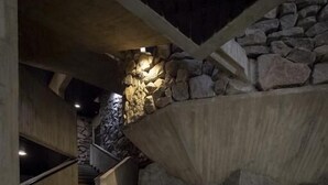 Una escalera con un muro de piedra a un lado y una barandilla de madera al otro, que lleva a un nivel superior.