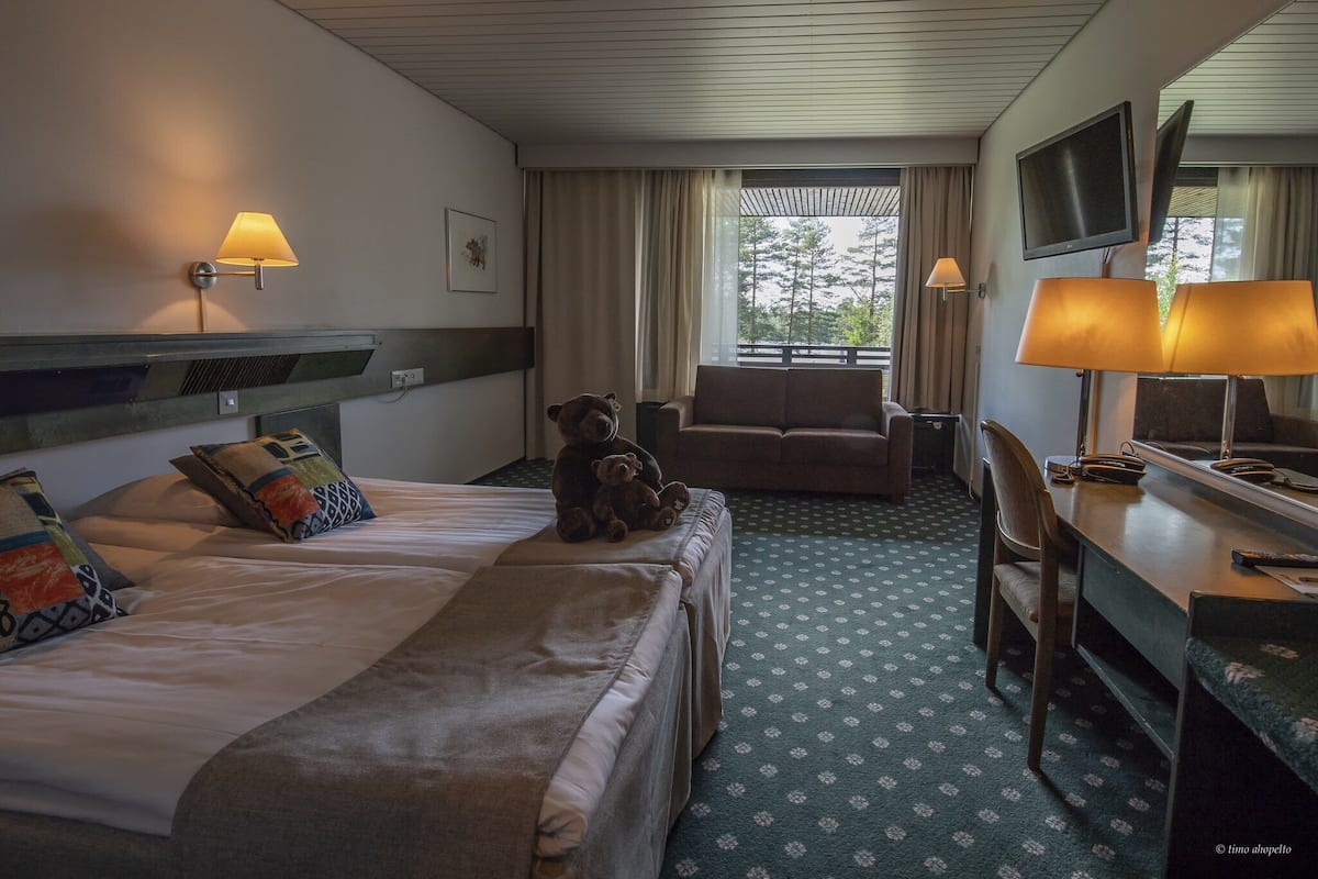 A hotel room with a bed, a sofa, a desk with a chair, a television, and a window with curtains.