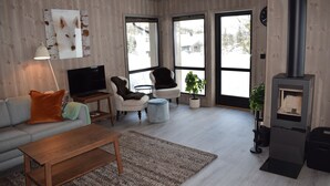 A modern living room with a sofa, coffee table, TV, fireplace, and large windows. - Skeikampen Booking (Gausdal)