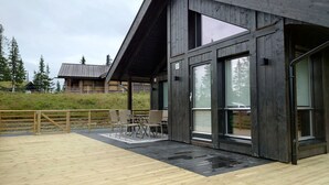 A modern wooden building with a covered patio area featuring outdoor seating. - Skeikampen Booking (Gausdal)