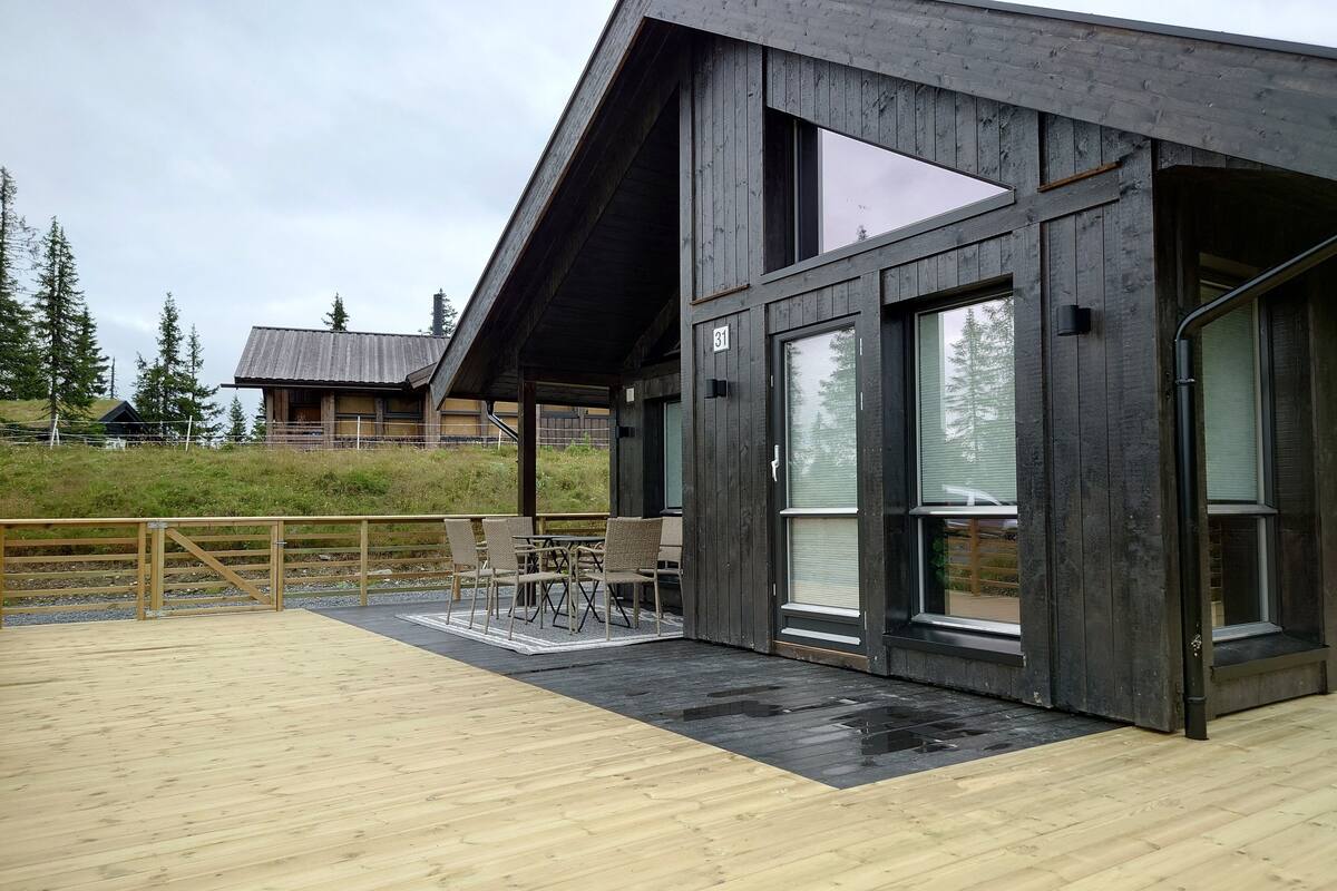 A modern wooden building with a covered patio area featuring outdoor seating.