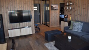 A modern living room with a flat-screen TV, wooden panel walls, a sofa, a coffee table, and a staircase leading to another room. - Skeikampen Booking (Gausdal)