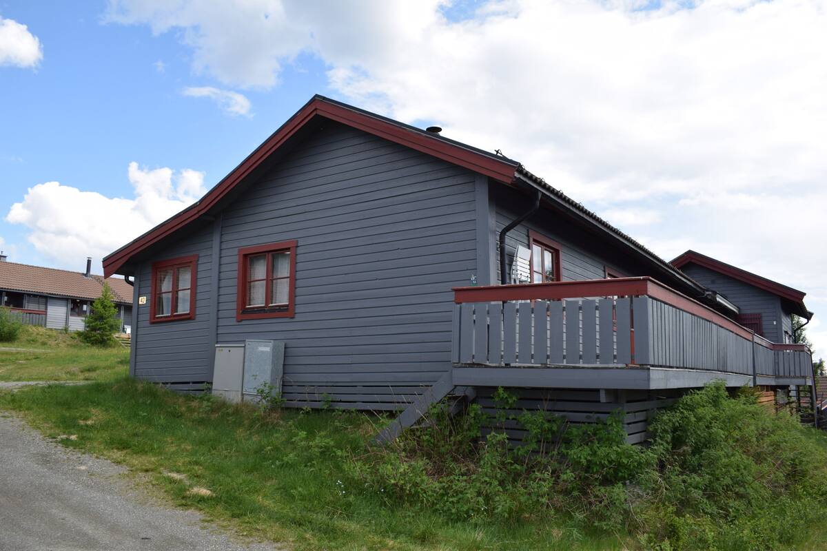 A two-story house with a red-framed window, a grey exterior, and a wooden deck.