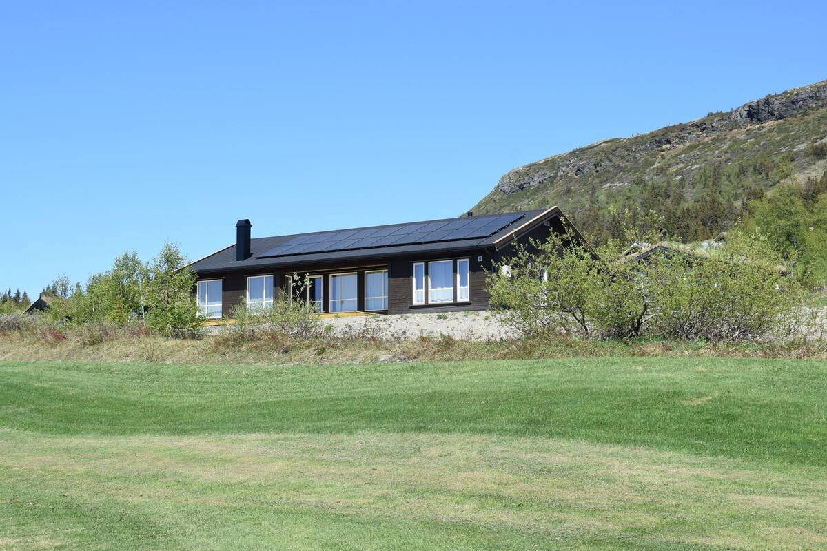 A modern house with a sloped roof, large windows, and a solar panel array.
