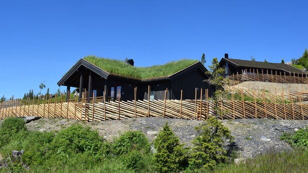 A modern building with a green roof, wooden fence, and a rocky landscape. - Skeikampen Booking (Gausdal)