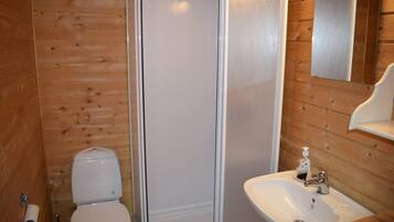 A bathroom with wooden walls, a toilet, a shower, and a sink with a mirror.