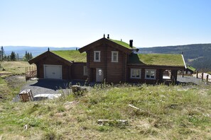 A wooden cabin with a garage, a covered porch, and a grassy hill in the background. - Skeikampen Booking (Gausdal)