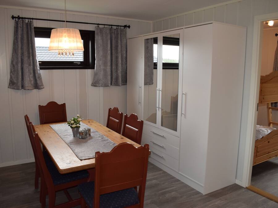 A dining area with a wooden table and chairs, a chandelier, and a wardrobe with a mirror.