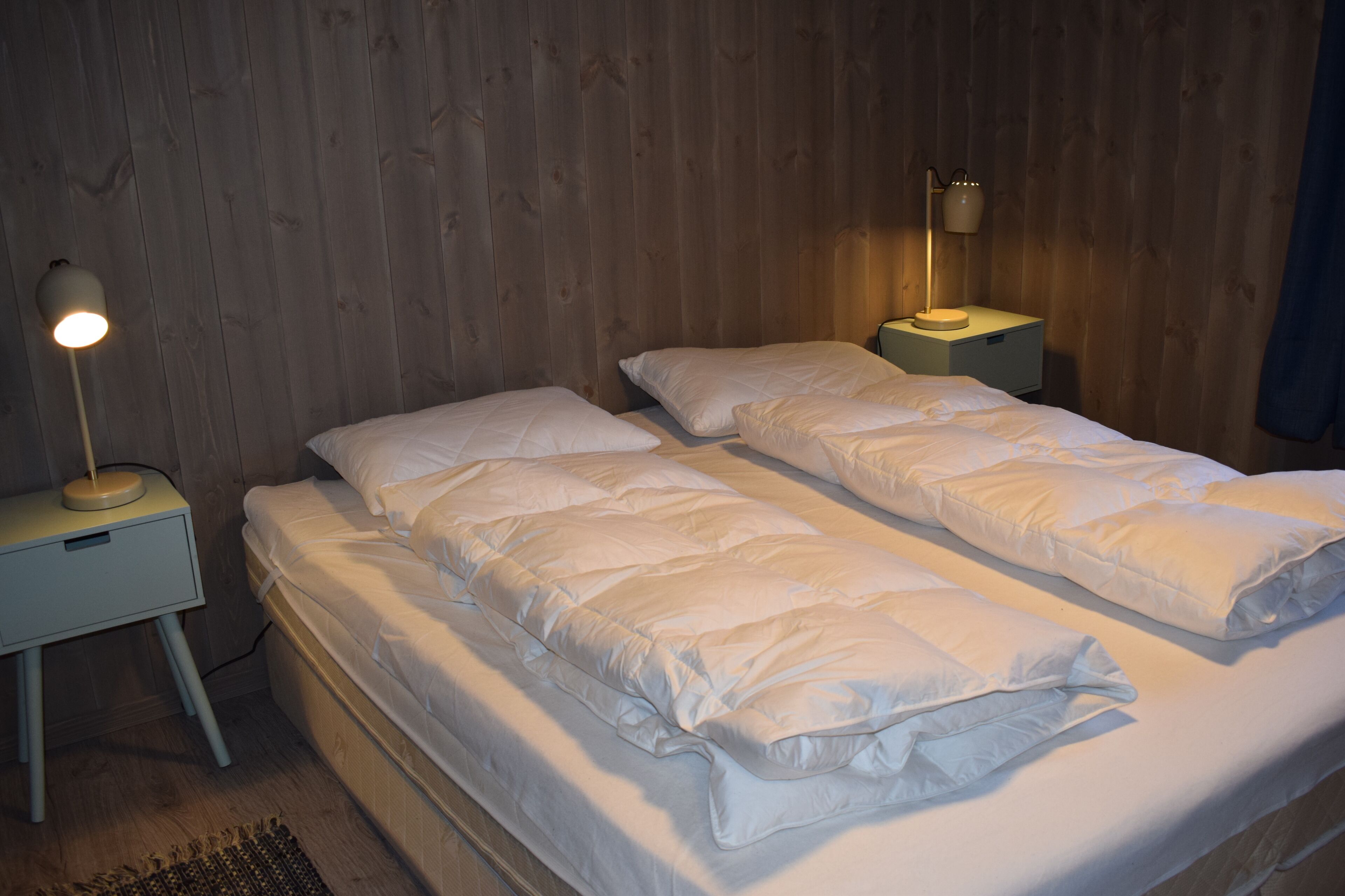 A double bed with white bedding in a room with wooden walls and two bedside tables with lamps.