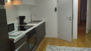 A compact kitchen with a microwave, stove, and sink. There is a door leading to another room.