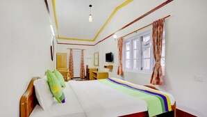 A hotel room with a bed, a desk, a chair, a television, and a window with curtains. - Treebo Atithi Bhavan, 1 Km From Ooty Lake (Ootacamund)