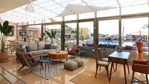 A spacious living area with a large window, a sofa, a coffee table, and a dining table with chairs. - Palms nº 11 -  Luxury Deluxe Four Bedroom Apartment (Ferragudo)