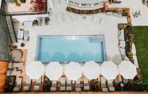 Ett poolområde på taket med en rektangulär pool, omgivet av trätrall, vita parasoller och planterade växter i krukor.