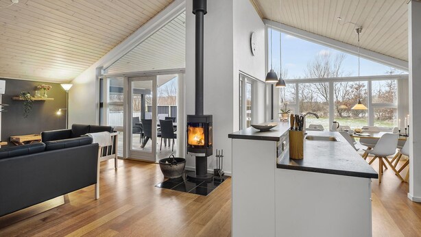 A modern interior with a central wood-burning stove, a dining area with natural light, and a cozy seating area.